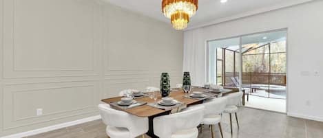Comedor con una gran mesa dispuesta para seis personas, sillas blancas, una araña y vistas amplias a través de ventanas grandes.