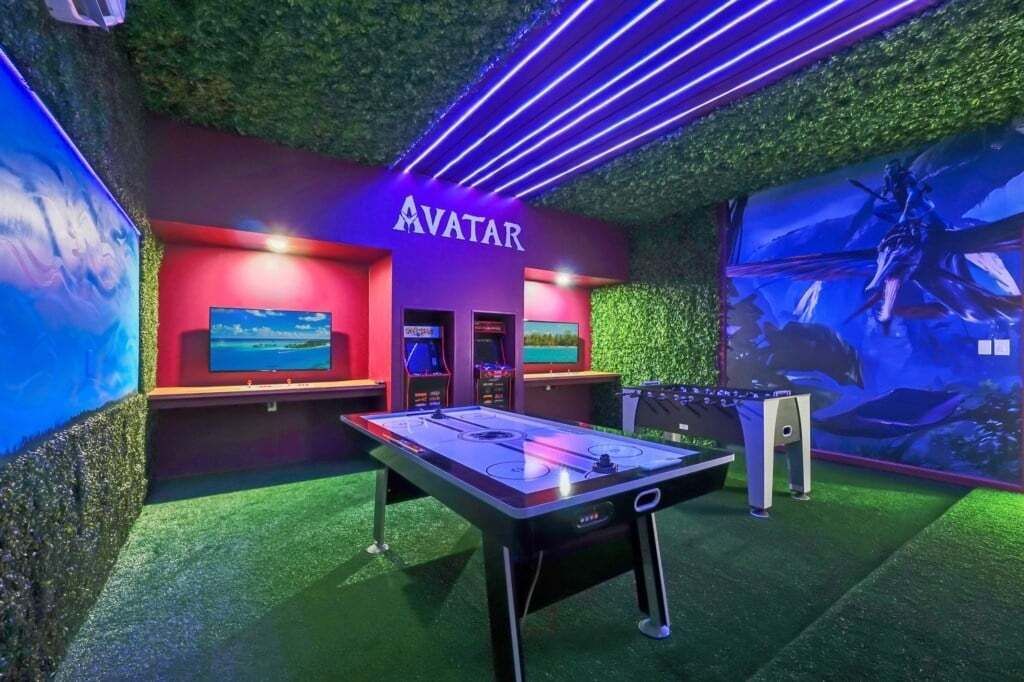 Une table de billard dans une pièce ornée d’un panneau indiquant « AVATAR », d’un gazon artificiel vert et d’une fresque murale.