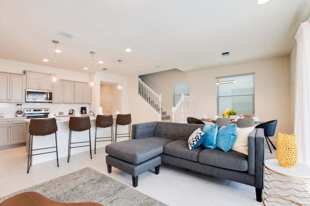 A modern kitchen with white cabinets, a microwave, and a dining area with a grey sofa and bar stools.