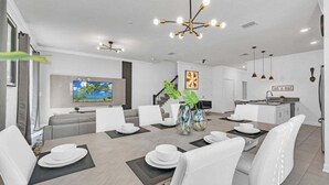 Een moderne eetruimte met een grote tafel voor vier personen, witte stoelen en een moderne kroonluchter.