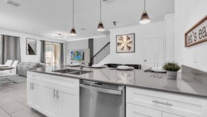 Een moderne keuken met witte kasten, roestvrijstalen apparatuur, hanglampen en een groot eiland.