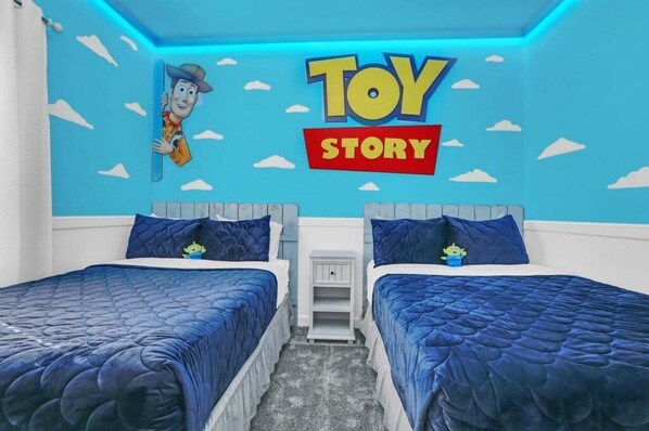 Une chambre avec deux lits, une fresque murale représentant des personnages du film « Toy Story », et une petite table de chevet.
