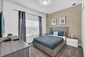 Une chambre à coucher avec un lit, des tables de chevet, un bureau et une fenêtre avec des rideaux.