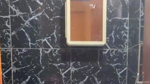 Une salle de bain avec un lavabo sur colonne blanc, des carreaux de marbre noir et un miroir au-dessus du lavabo.