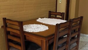 Une table à manger avec quatre chaises en bois, une nappe en dentelle blanche et un mur de briques sur lequel est accroché un panneau indiquant : « BIRDS OF A FEW VENIENDOS ».