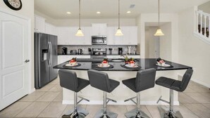 A modern kitchen with white cabinets, a central island with bar stools, stainless steel appliances, and pendant lighting. - Lake View Serene & Peaceful Pool Home! 5 Bedroom Townhouse (Kissimmee)