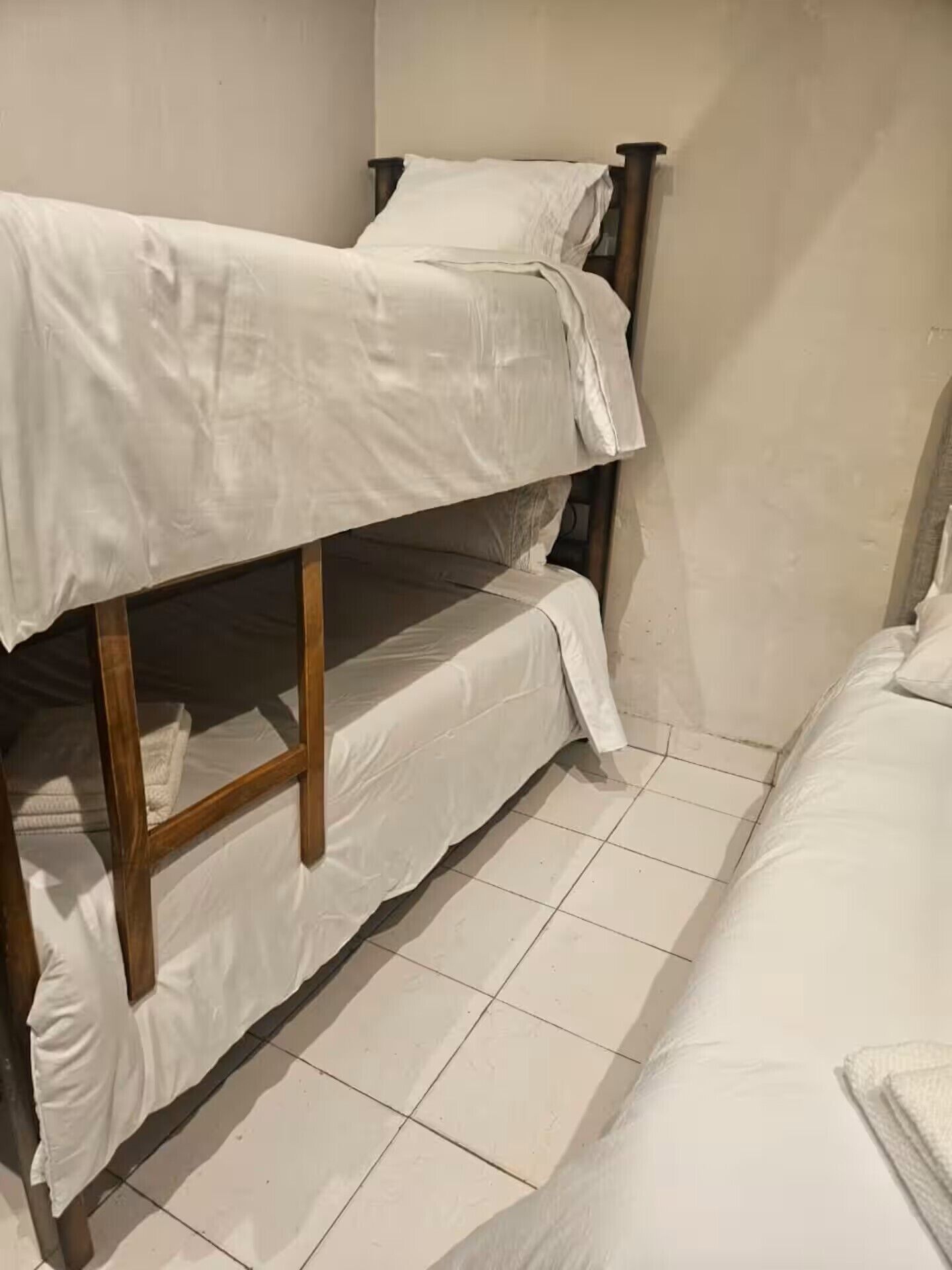 Uma cama beliche com roupa de cama branca em um quarto com piso de azulejo.