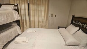 Una habitación de hotel con una cama grande, dos camas más pequeñas y una mesita de noche.