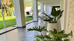 Un espacio exterior cubierto con plantas en macetas, un patio con sillas y vistas a un jardín.