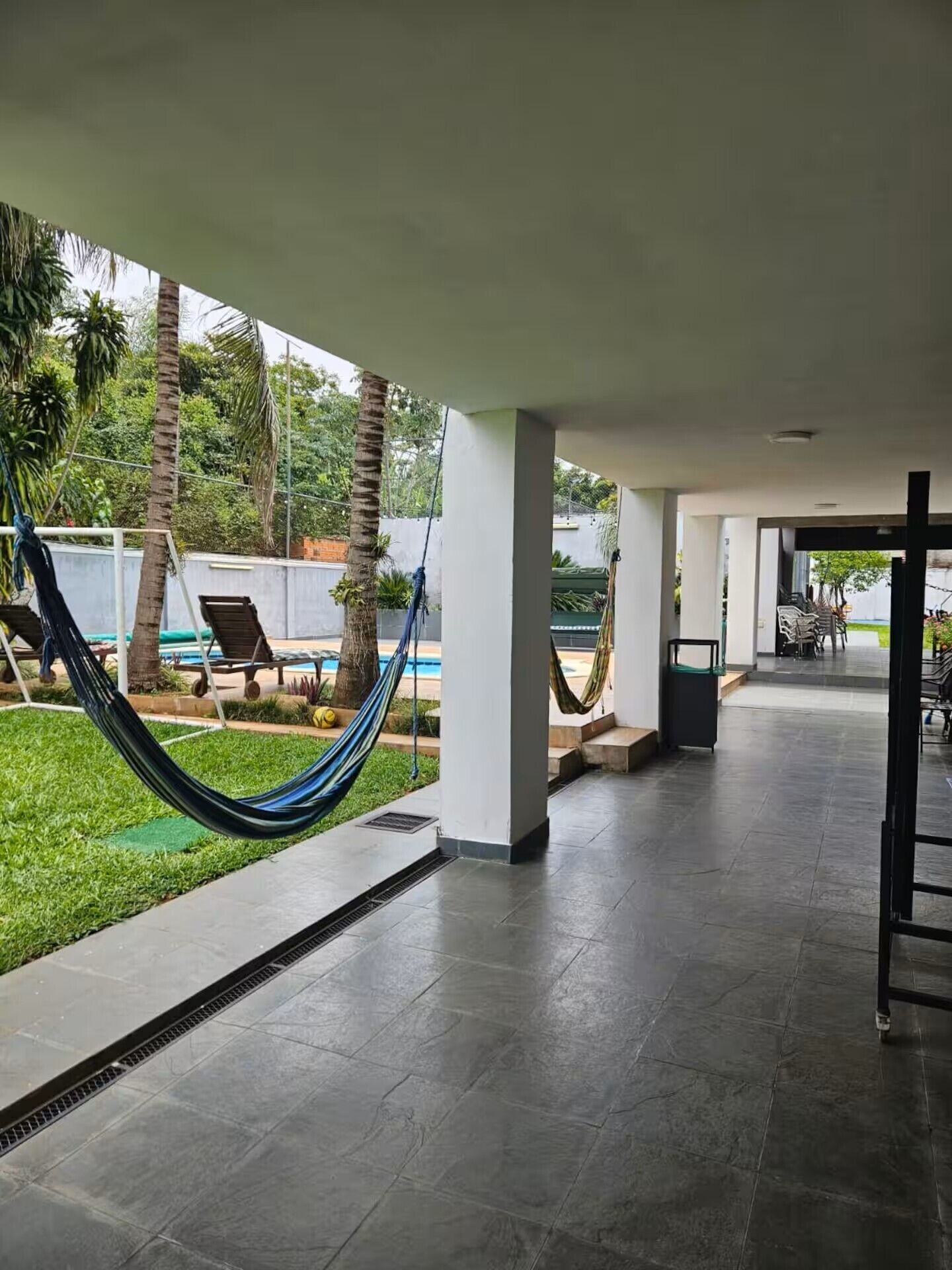 Uma área externa ampla com piscina, palmeiras e uma rede.