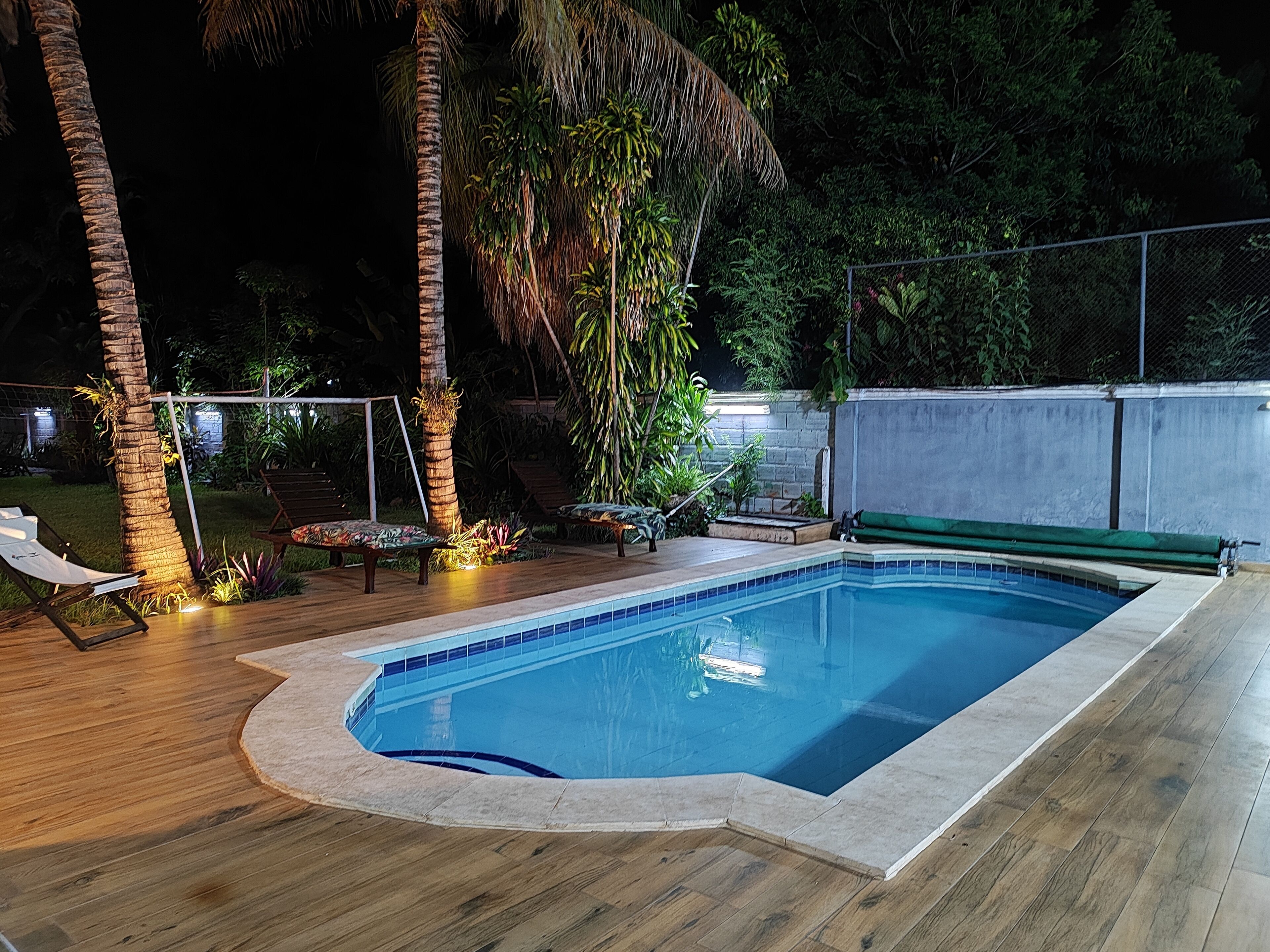 Uma piscina retangular com borda revestida em azulejo, cercada por um deck de madeira.