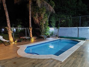A rectangular swimming pool with a tiled edge, surrounded by a wooden deck.