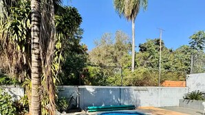 Una piscina con cubierta de madera, sillas de descanso y palmeras.