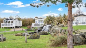 Un camping con dos casas móviles, una cascada pequeña y una zona de césped con rocas.