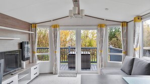 Una habitación acogedora con televisor, sofá y balcón con vistas a árboles.