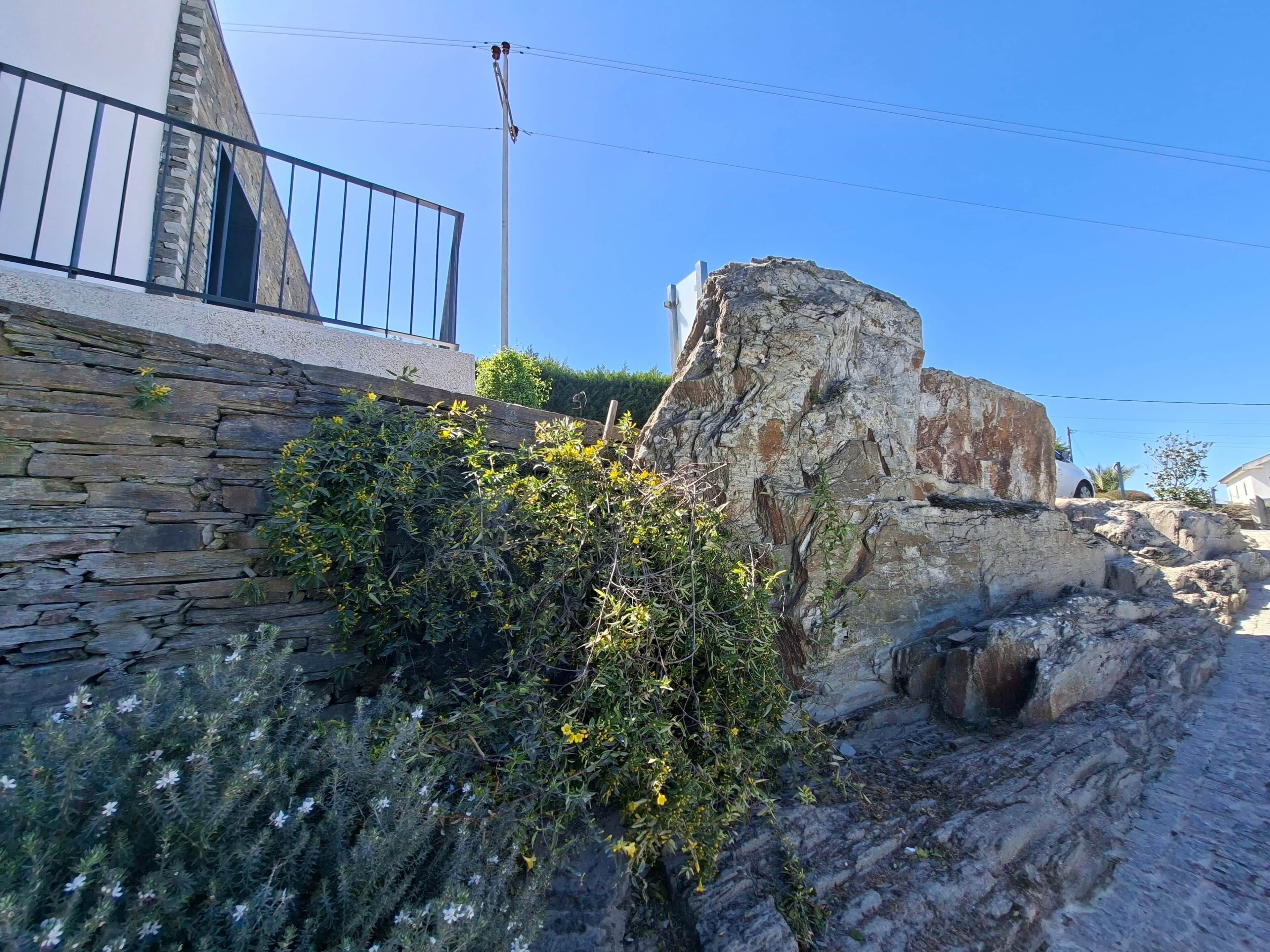 A stone wall with vegetation, a metal railing, and a clear blue sky.