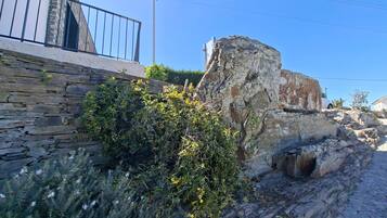A stone wall with vegetation, a metal railing, and a clear blue sky.
