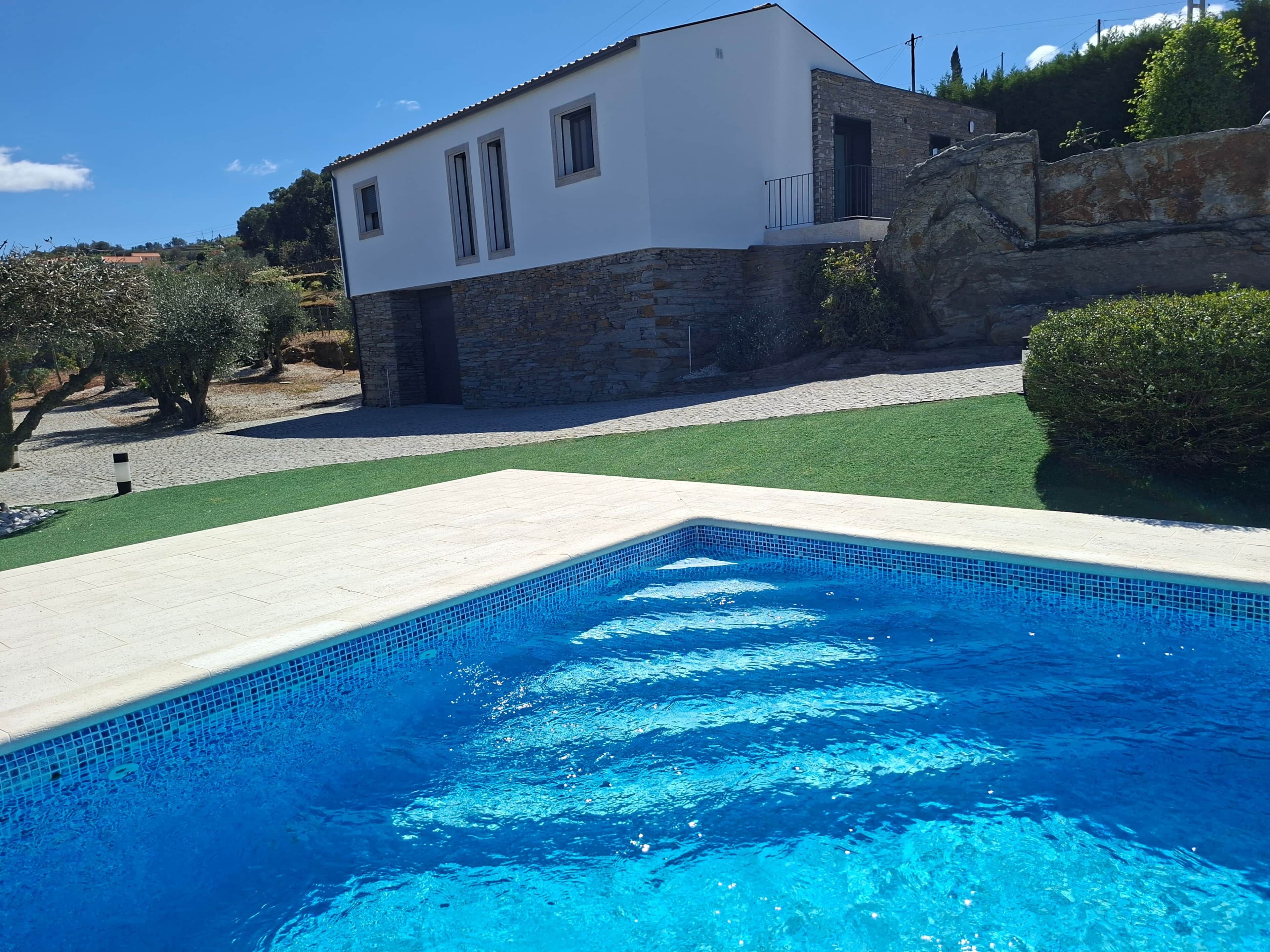 A modern house with a swimming pool, stone walls, and a well-maintained lawn.