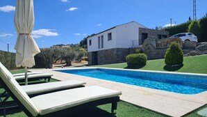 A swimming pool with lounge chairs and an umbrella, a stone wall, and a modern house in the background. - The Douro Nest — Casa com Piscina Privada perto de Pinhão (Valença do douro)