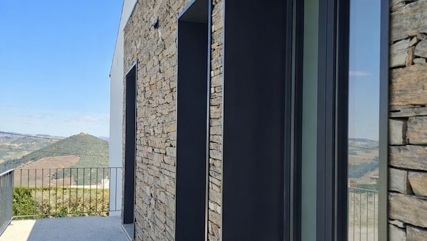 A modern building with stone facade, large glass windows, and a balcony with a view of the countryside. - The Douro Nest — Casa com Piscina Privada perto de Pinhão (Valença do douro)