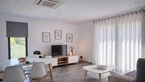 A modern living room with a dining area, a flat-screen TV, and a large window with sheer curtains. - The Douro Nest — Casa com Piscina Privada perto de Pinhão (Valença do douro)