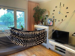 Un salon moderne avec un hamac, une grande fenêtre, une horloge murale et un téléviseur à écran plat.