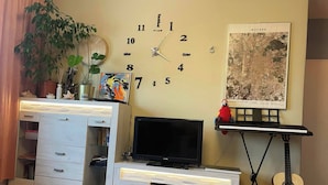 Een woonkamer met een witte entertainmentkast, een flatscreen televisie, een gitaarstandaard en een wandklok.