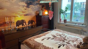 Een slaapkamer met een bed, een dressoir, een nachtkastje, een lamp, een raam met uitzicht en een muurschildering.