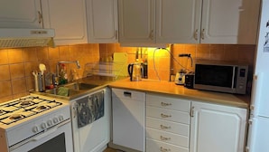 Een keuken met witte kasten, een gasfornuis, een vaatwasser, een magnetron en een spoelbak.