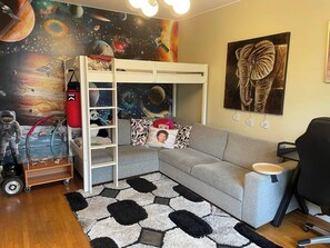Ein Kinderzimmer mit Etagenbett, einer Wandmalerei zum Thema Weltall, einem Panda-Plüschtier und einem großen Elefantenbild.