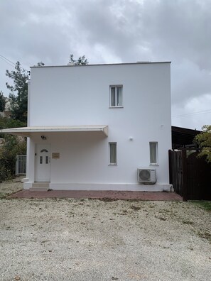 A white two-story building with a covered entrance, a small window, and an air conditioning unit. - Villa Eldora Lysos With Beautiful pool (Lysos)