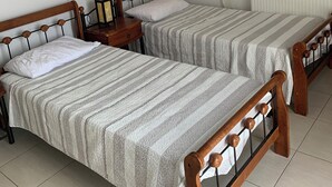 Ein Zimmer mit zwei Einzelbetten, einem Nachttisch mit Lampe, einem Heizkörper und einem Fenster mit Vorhängen.