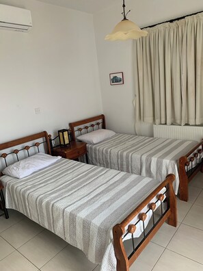 A room with two single beds, a bedside table with a lamp, a radiator, and a window with curtains. - Villa Eldora Lysos With Beautiful pool (Lysos)