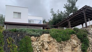 A modern house with a stone retaining wall, a white exterior, and a covered outdoor area.