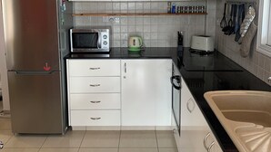 Eine Küche mit weißen Schränken, einem Edelstahlkühlschrank, einer Mikrowelle, einem Wasserkocher und einem Spülbecken.