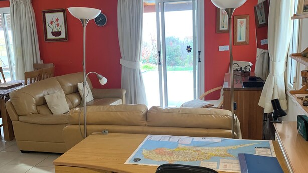 Ein Wohnzimmer mit einer Couch, einem Schreibtisch mit Stuhl, einem Deckenventilator und einem großen Fenster mit Vorhängen.