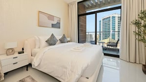 Habitación de hotel moderna con una cama grande, una mesita de noche con lámpara y vista a un paisaje urbano a través de un ventanal.