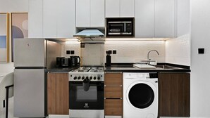 Cocina compacta con estufa integrada, microondas y lavadora, con armarios blancos y encimera negra.