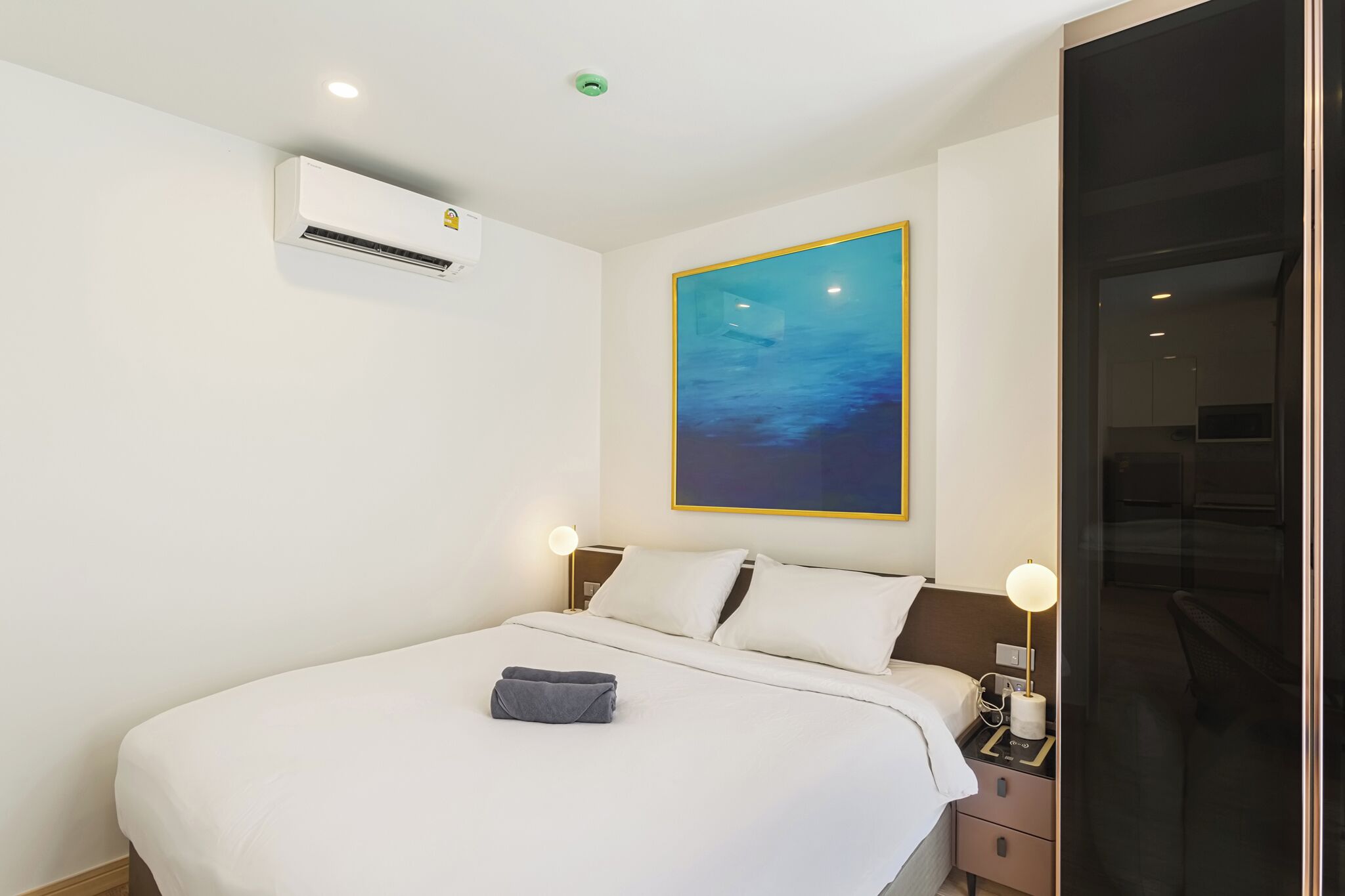 Habitación de hotel con cama, lámparas de noche, un equipo de aire acondicionado y un cuadro en la pared.