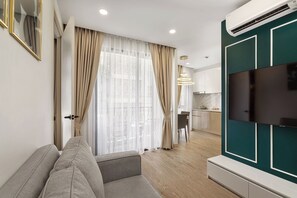 A modern living room with a sofa, a flat-screen TV mounted on a teal wall, and a kitchen in the background. - One bedroom Palmetto Condo Karon A309 (Karon)