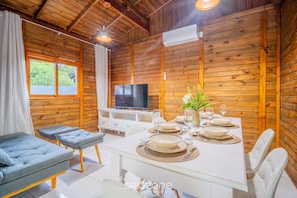 L’intérieur d’un chalet en bois comprend une table à manger pour quatre personnes, un canapé, un téléviseur et un appareil de climatisation.