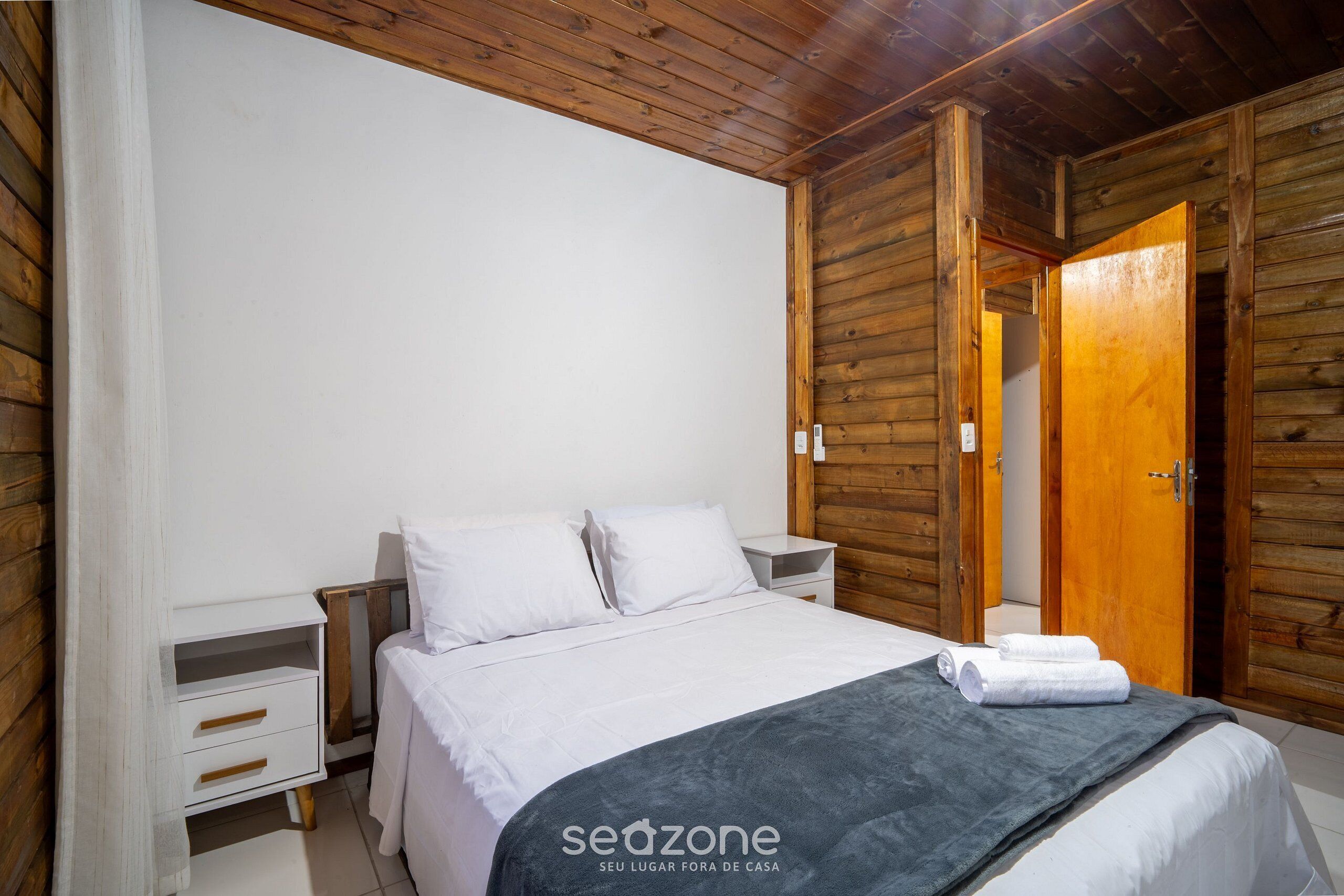 A bedroom with a wooden ceiling, a bed with white bedding, a nightstand, and a wooden wardrobe.