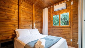 A wooden cabin room with a bed, a window with curtains, and an air conditioning unit. - Wooden Retreat Near Lagoa da Conceicao Knu0170 (Florianópolis)