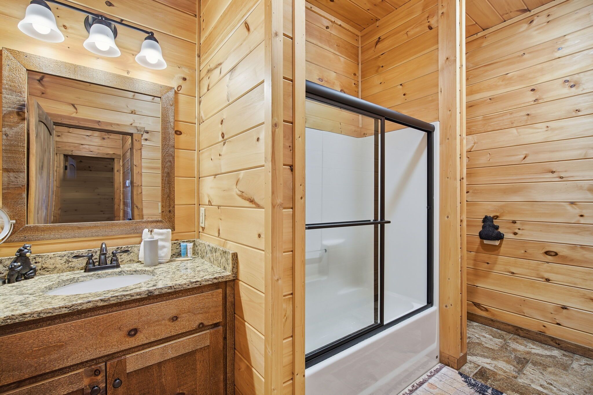 Un baño de cabaña de madera con lavamanos, espejo y ducha.