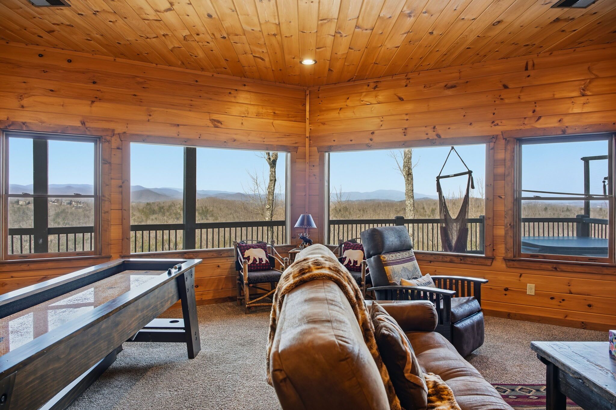 Una cabaña de madera con mesa de billar, sofá de cuero y grandes ventanales que ofrecen vistas a las montañas.