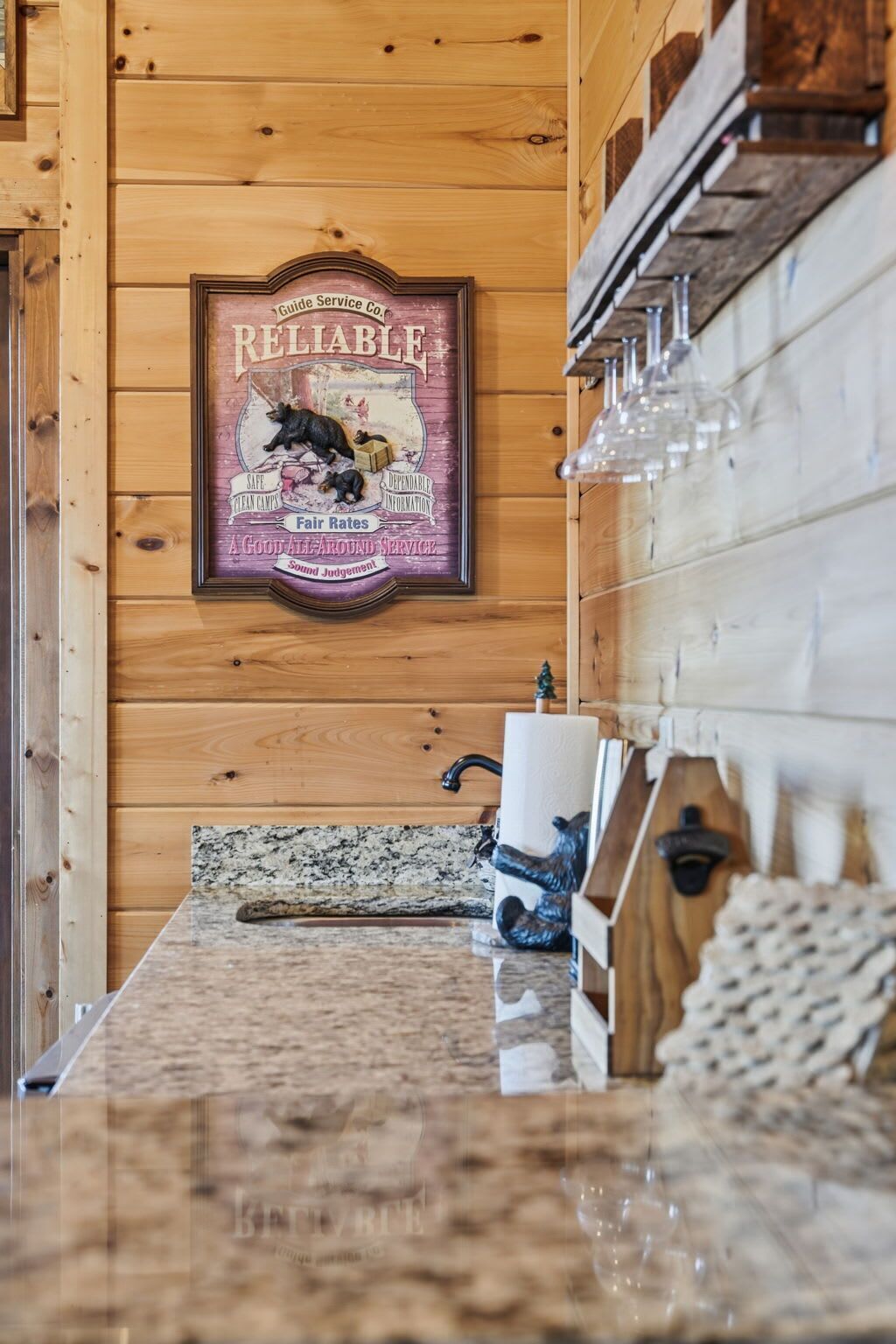 A wooden cabin interior with a kitchen area, a framed sign on the wall, and a granite countertop.