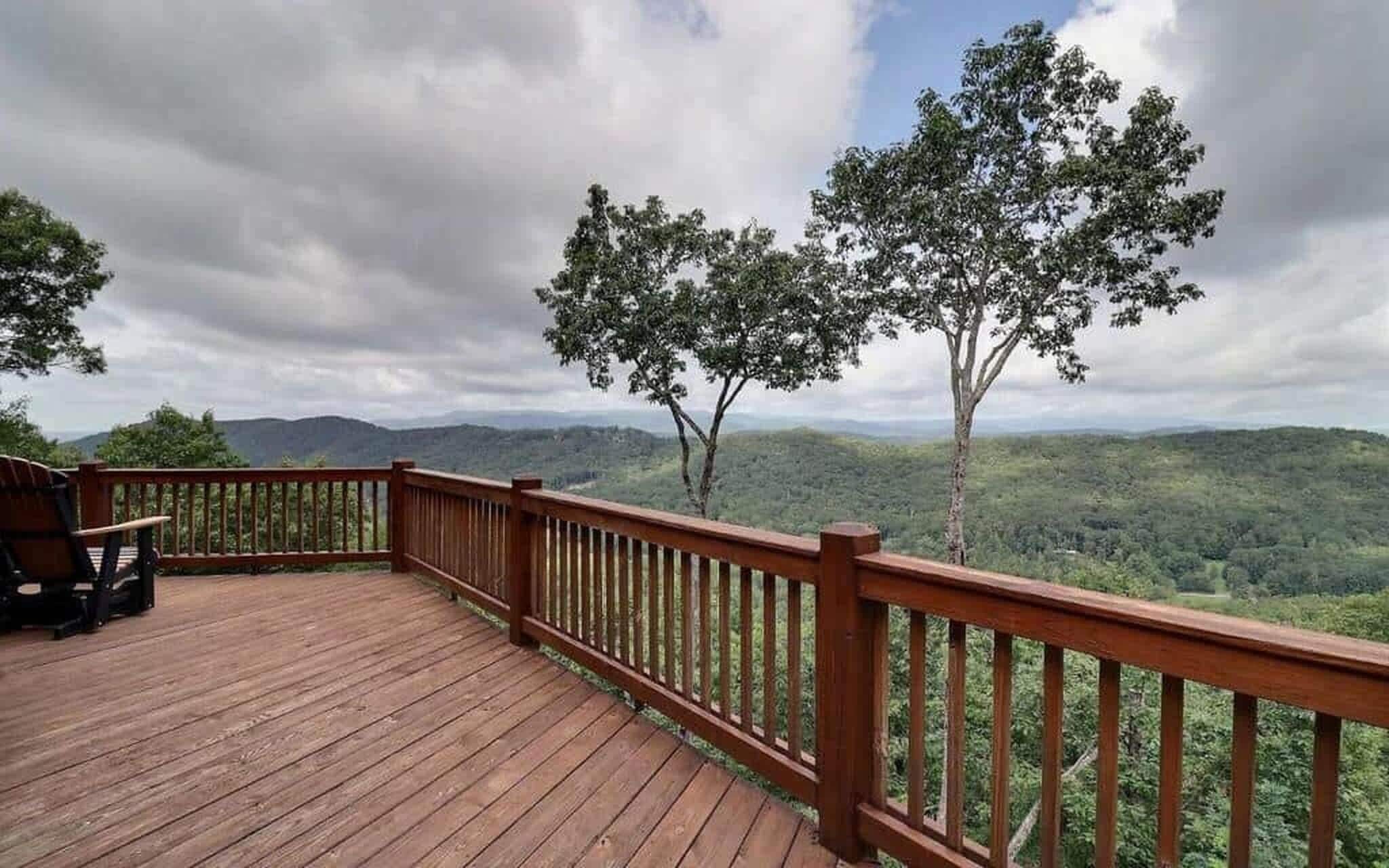 Una terraza de madera con barandilla que da a un paisaje boscoso con colinas a lo lejos.