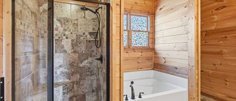 Baño de cabaña de madera con ducha envuelta en vidrio, una bañera blanca y una pequeña ventana con vitrales.