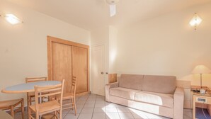 Una habitación con una mesa de comedor de madera, sillas, un sofá beige y una pequeña mesita de noche con una lámpara.