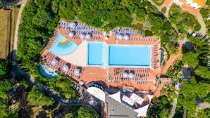 Vista aérea de un resort con múltiples piscinas, sillas de sol y una zona circular central con una fuente.